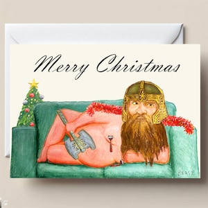 Puede incluir: Una tarjeta de Navidad humorística con una ilustración en acuarela. La tarjeta representa una figura con casco y barba, sosteniendo un hacha, reclinada en un sofá verde. El texto "Merry Christmas" está escrito en la parte superior. Un pequeño árbol de Navidad está a la izquierda.