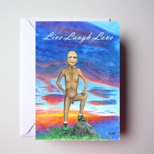 May include: A greeting card featuring a drawing of a nude man standing on a rock against a sunset backdrop. The card reads "Live Laugh Love" and is signed "Beave".