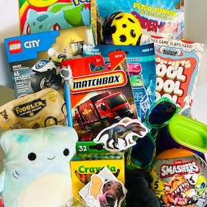 May include: A collection of children's toys and books including a Crayola Pokemon coloring book, a Lego City police motorcycle set, a Matchbox fire truck, a Fuggler bag clip, a plush shark, Smashers dinosaur eggs, green sunglasses, and stickers.