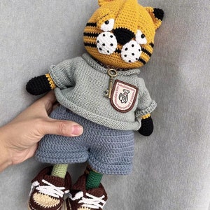 May include: A handmade crochet tiger doll wearing a gray sweater, blue shorts, and brown and white sneakers. The tiger has a yellow head with black stripes and white spots. A key-shaped charm hangs from its neck. The doll is approximately 12 inches tall.