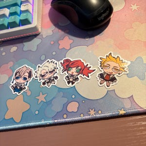 Może przedstawiać: Cztery naklejki z postaciami w stylu anime o r&oacute;żnych wzorach. Naklejki przedstawiają postacie o r&oacute;żnych kolorach włos&oacute;w i strojach. Naklejki znajdują się na pastelowej podkładce pod mysz ze wzorami gwiazd i chmur. Widoczna jest r&oacute;wnież czarna mysz komputerowa i klawiatura.