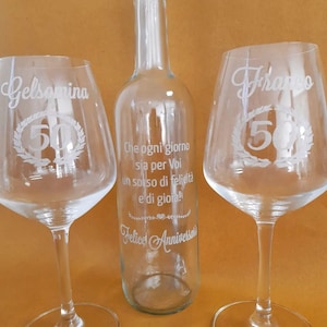 Può includere: Due bicchieri da vino in vetro trasparente con i nomi Gelsomina e Franco incisi, ognuno con una corona e il numero 50. Una bottiglia di vetro trasparente con il testo "Che ogni giorno sia per Voi un sorso di felicità e di gioia!" e "Felice Anniversario" inciso.