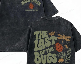 Può includere: Una t-shirt grigio antracite con lavaggio acido che presenta una grafica frontale con il testo Noah Kahan e The Great Divide sopra una coccinella. Il retro mostra il testo The Last Of The Bugs e Call Me When The Bugs Don't Die con illustrazioni.
