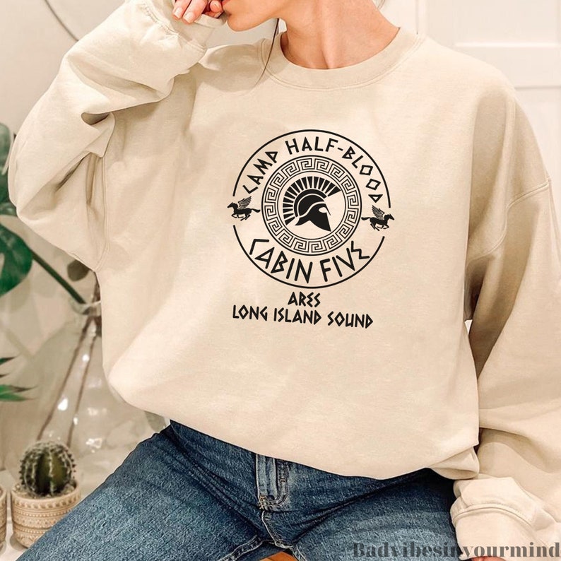 May include: A beige sweatshirt with a black graphic design featuring a Greek helmet, a winged horse, and the text "Camp Half-Blood Cabin Five Ares Long Island Sound".