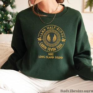 May include: A dark green sweatshirt with a gold graphic of a pegasus and the text "Camp Half-Blood Cabin Seven Teen Nike Long Island Sound".