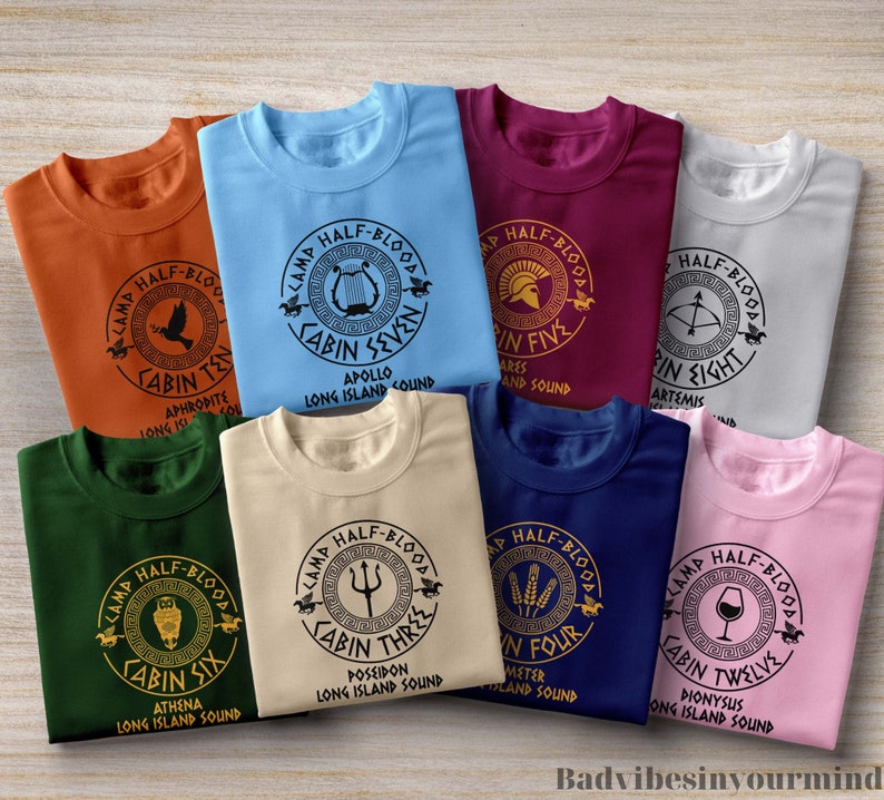 May include: Ten different t-shirts with a Camp Half-Blood logo. Each shirt features a different cabin number and Greek god name. The shirts are in various colours, including orange, blue, maroon, grey, green, beige, navy blue, and pink.