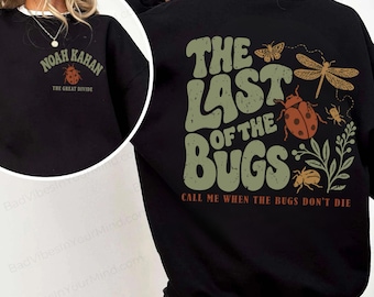 Può includere: Una felpa nera a girocollo con una piccola grafica frontale raffigurante una coccinella e il testo "Noah Kahan The Great Divide". Il retro presenta una grande grafica con il testo "The Last of the Bugs" e "Call Me When the Bugs Don't Die", accompagnata da illustrazioni di una libellula, una coccinella e vari insetti.