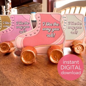 May include: Roller skate-shaped cards in pink, peach, and blue with the text "I like the way you roll!" and chocolate candies. A pink circle with the words "instant DIGITAL download" is in the foreground. The cards are on a wooden surface.