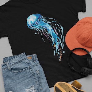 May include: A black t-shirt with a watercolor illustration of a blue jellyfish. The jellyfish has long, flowing tentacles and is surrounded by a few small white dots.