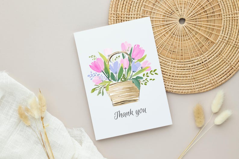 May include: A white greeting card with a watercolor illustration of a basket filled with pink and purple tulips and green foliage. The words "Thank you" are written below the illustration.