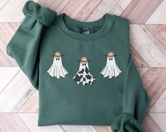 May include: Forest green unisex heavy blend sweatshirt featuring three ghost figures wearing cowboy hats. One ghost has a black and white cow print. The sweatshirt is from the brand Gildan 18000.