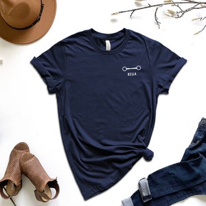 May include: A navy blue t-shirt with a white horse bit and the name "Bella" printed on the front.