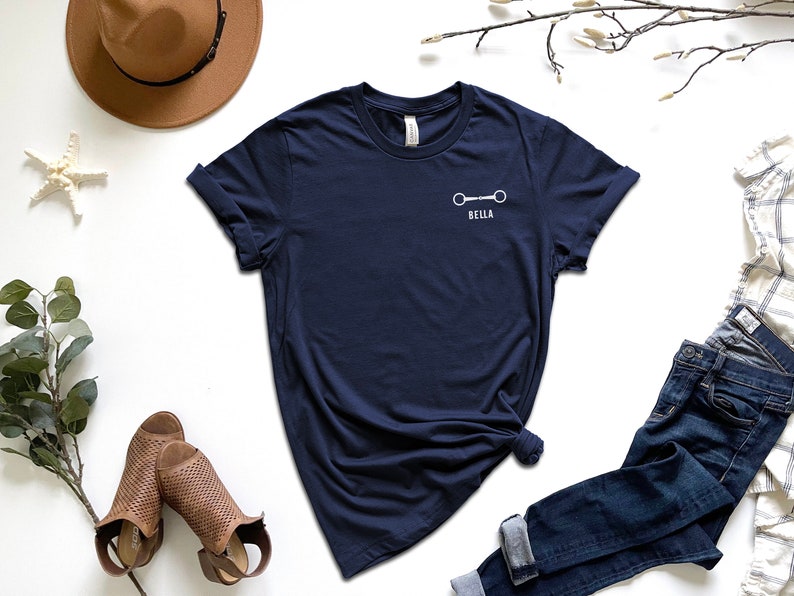 May include: A navy blue t-shirt with a white horse bit and the name "Bella" printed on the front.