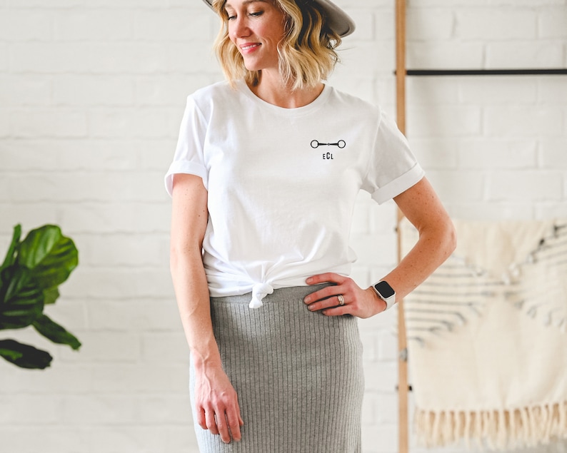 May include: White t-shirt with a black equestrian bit design and the text "EQL" underneath.