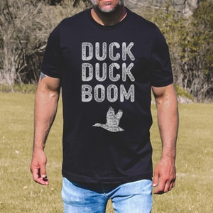 May include: Black t-shirt with a white distressed graphic that says "Duck Duck Boom" and a white silhouette of a flying duck.