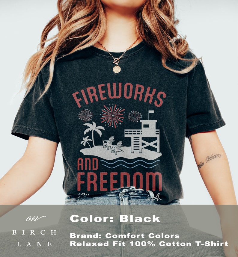May include: Black t-shirt with a graphic design featuring the words "FIREWORKS AND FREEDOM". The design includes fireworks, palm trees, a lifeguard tower, and beach chairs. Made of 100% cotton.