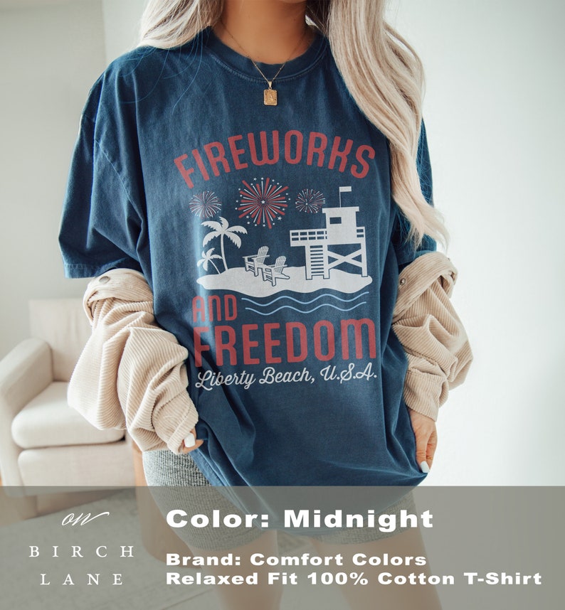 May include: Midnight blue t-shirt with a graphic that reads "Fireworks and Freedom" above a beach scene with a lifeguard tower and palm trees. The text "Liberty Beach, U.S.A." is below the graphic. The shirt is a relaxed fit.