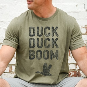May include: A green t-shirt with a distressed black graphic that reads "Duck Duck Boom" and a silhouette of a duck flying above the text.