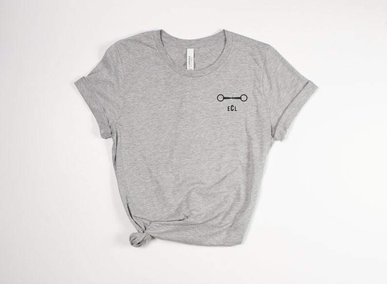 May include: A gray t-shirt with a black equestrian bit and the letters "ECL" printed on the front.