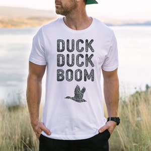 May include: White t-shirt with a black graphic print that says "Duck Duck Boom" and a silhouette of a duck flying.