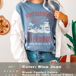 May include: Blue jean colored t-shirt with the words "Fireworks and Freedom" in red. The graphic includes fireworks, palm trees, a lifeguard tower, and the text "Liberty Beach, U.S.A."