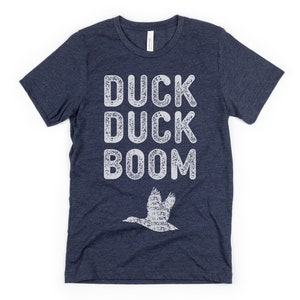 May include: A navy blue t-shirt with a white distressed graphic that says "Duck Duck Boom" and a white silhouette of a duck flying above the text.