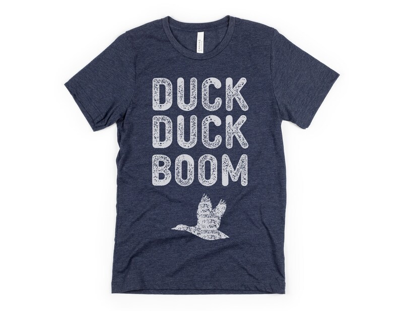 May include: A navy blue t-shirt with a white distressed graphic that says "Duck Duck Boom" and a white silhouette of a duck flying above the text.