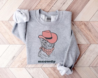 Puede incluir: Sudadera gris con un gráfico de un gato con un sombrero de vaquero rosa y un pañuelo. El texto "meowdy" está impreso debajo del gato.