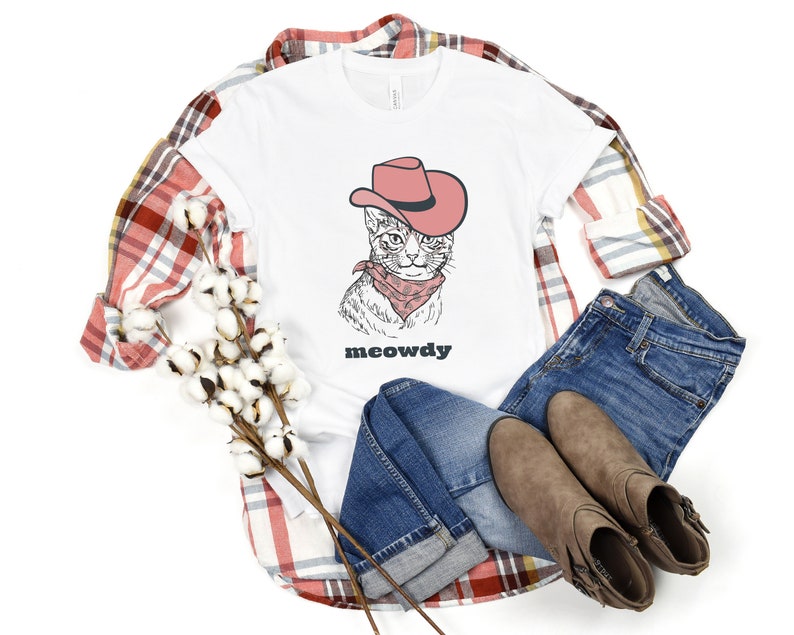 May include: White t-shirt with a cartoon illustration of a cat wearing a cowboy hat and bandana. The text "meowdy" is printed below the cat.