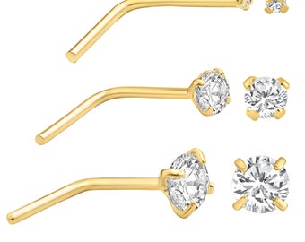 May include: Three gold-colored nose studs with clear, round, sparkling gemstones. The studs have a curved post design. Two additional gemstones are shown separately. The jewelry is displayed against a white background.