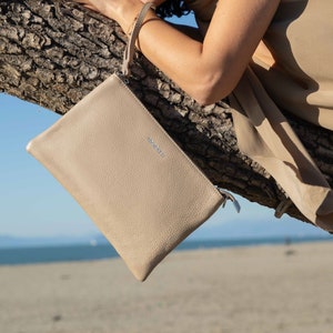 a woman leaning on a tree branch holding a purse