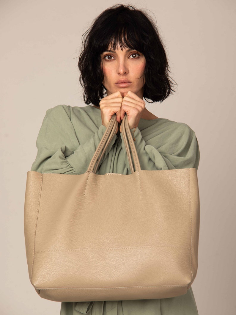 a woman is holding a large beige bag