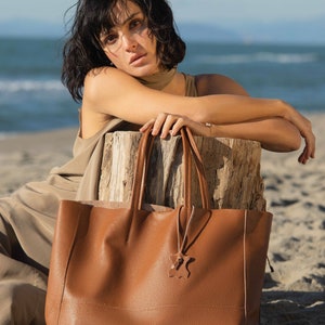 a woman sitting on the beach with a brown bag