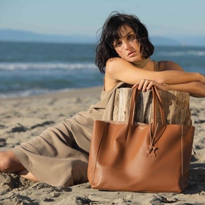 a woman sitting on the beach with a brown bag