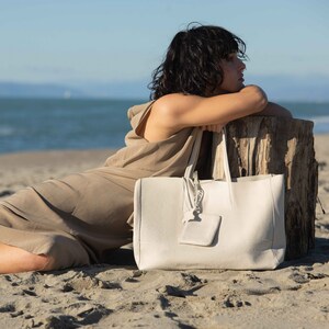 a woman sitting on the beach with a white bag