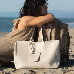 a woman sitting on the beach with a white bag