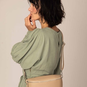 a woman in a green dress is holding a beige purse