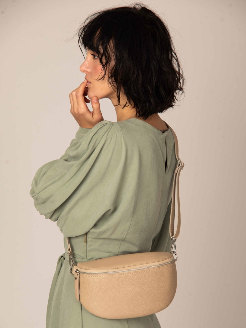 a woman in a green dress is holding a beige purse