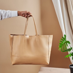 a person holding a tan leather tote bag