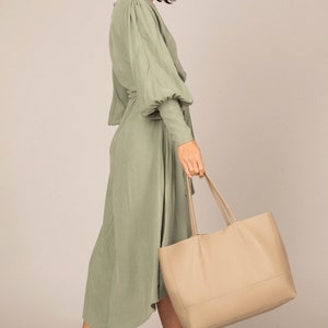 a woman in a green dress carrying a beige bag