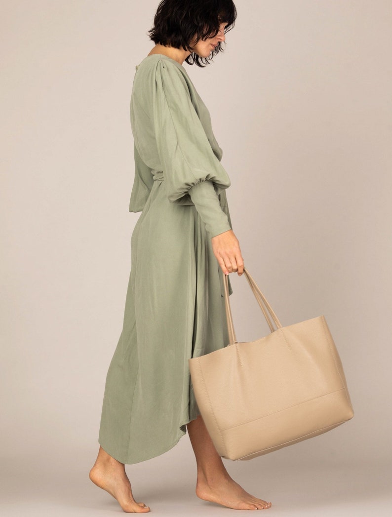 a woman in a green dress carrying a beige bag