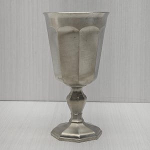 May include: A white ceramic mug with a black handle and the text "But First, Coffee" in a bold, black font. The mug is set against a blurred background, suggesting a cozy setting.