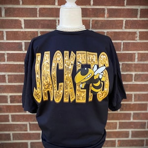 May include: Black t-shirt with gold glitter lettering that says "JACKETS" and a cartoon bee with black and yellow stripes.