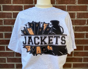 Peut inclure: Un t-shirt gris avec un graphique noir et orange d'un mégaphone avec le mot "JACKETS" imprimé dessus.