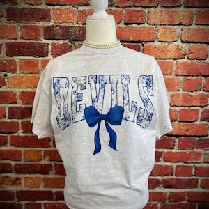 May include: A gray t-shirt with a blue floral pattern spelling out "DEVILS" with a blue bow in the center.
