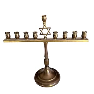 May include: A brass menorah with nine candle holders and a Star of David in the center. The base is round, and the candle holders are small cylinders. The menorah is a traditional Jewish symbol.