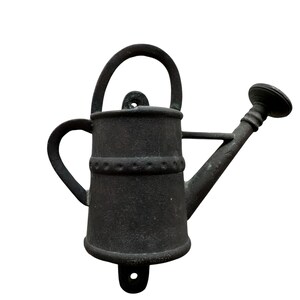 May include: A dark gray metal watering can with a handle, spout, and side handle. The watering can has a decorative band around the middle and a hole for mounting. The design is rustic and suitable for garden decor.