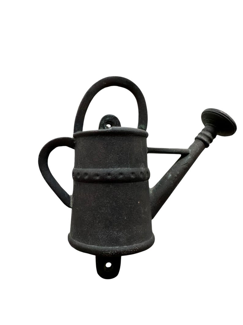 May include: A dark gray metal watering can with a handle, spout, and side handle. The watering can has a decorative band around the middle and a hole for mounting. The design is rustic and suitable for garden decor.