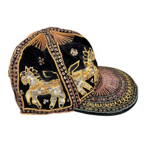 May include: A black velvet baseball cap featuring intricate gold and silver metallic embroidery depicting horses. The cap is adorned with decorative sequins and beadwork along the seams and the brim, showcasing detailed craftsmanship throughout.