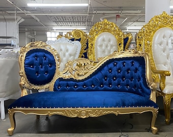 May include: A blue velvet chaise longue with gold-painted wood carvings and a tufted back. The chaise longue has a curved shape and is decorated with gold nailhead trim.
